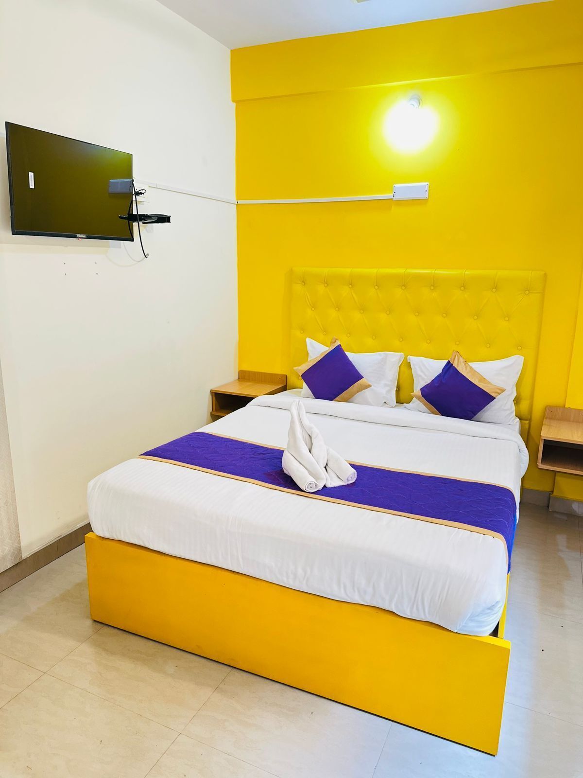 Een hotelkamer met een bed, een aan de muur bevestigde televisie en een nachtkastje.