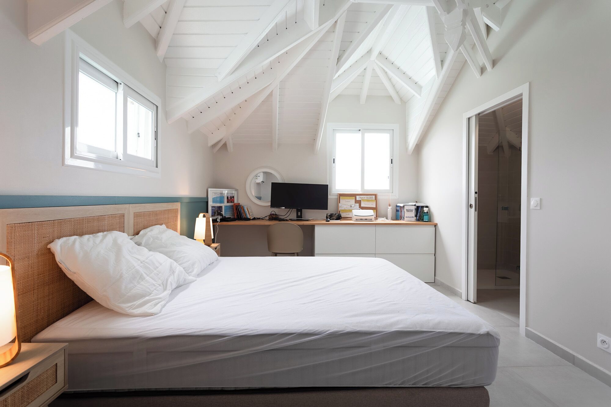 A bedroom with a bed, desk, and computer. There are windows and a door.