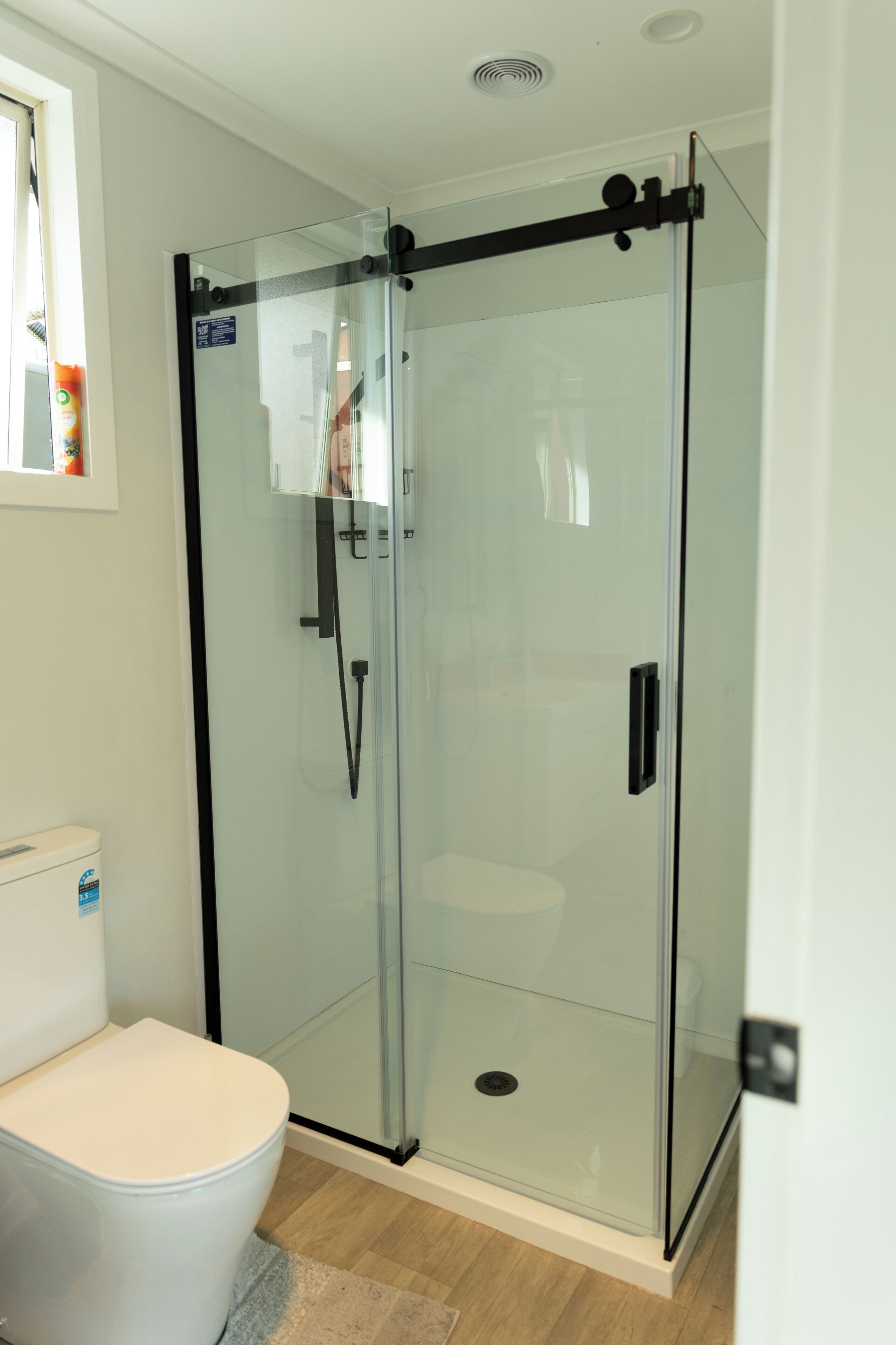 Een badkamer met een douchecabine van glas, een wit toilet en een zichtbare douchepaneel.