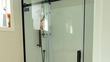 Een badkamer met een douchecabine van glas, een wit toilet en een zichtbare douchepaneel.
