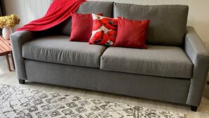 A grey sofa with two red pillows and a red throw blanket. - Punga Grove - Bush setting, kayaking, Trout fishing, Waterfalls, Glow worms (Omanawa)