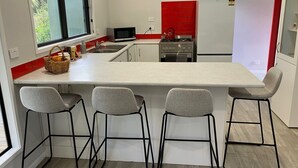 A compact kitchen with a central island, three bar stools, a microwave, a stove, and a refrigerator. - Punga Grove - Bush setting, kayaking, Trout fishing, Waterfalls, Glow worms (Omanawa)