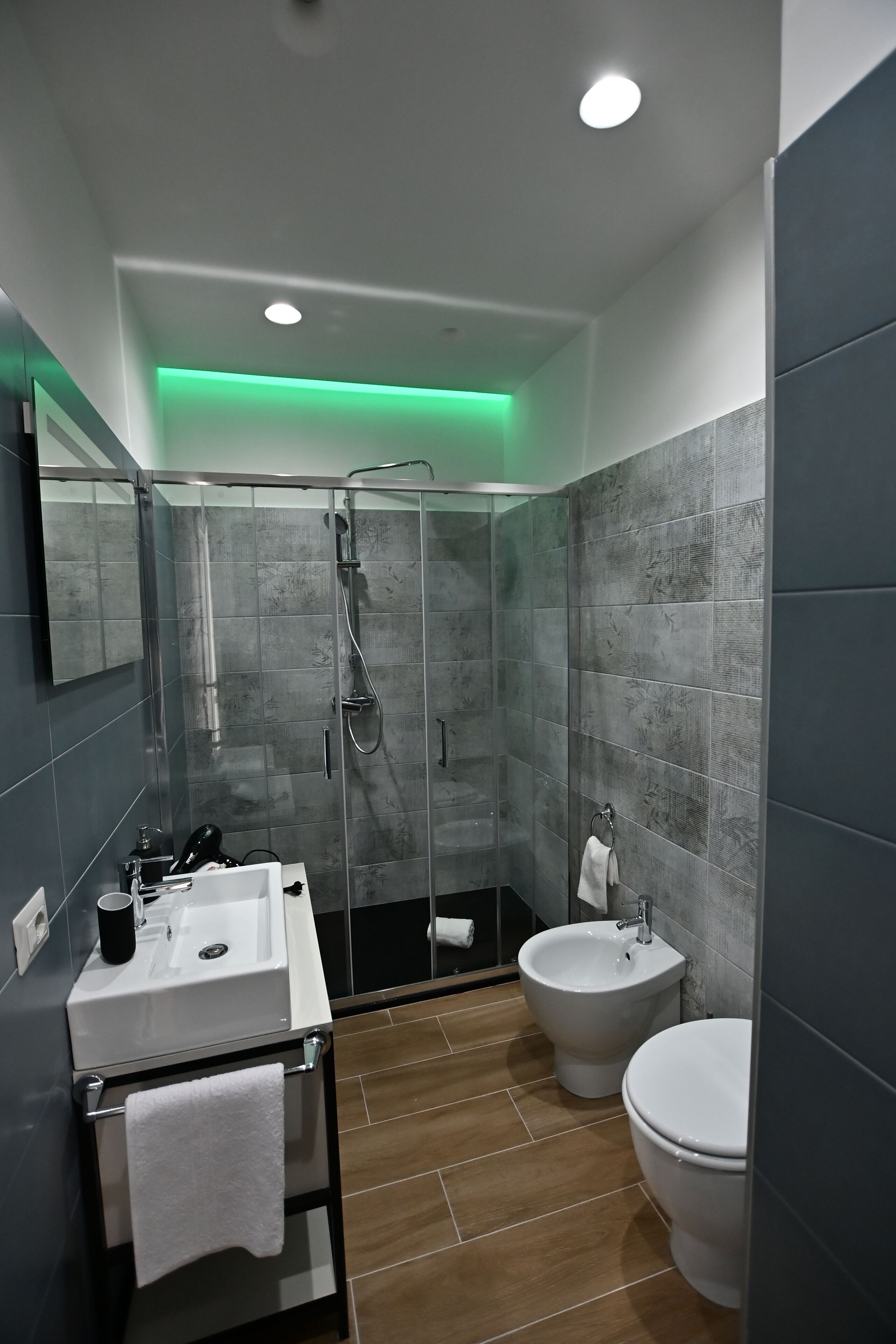 A modern bathroom with a glass-enclosed shower, a white sink, a bidet, and a toilet.