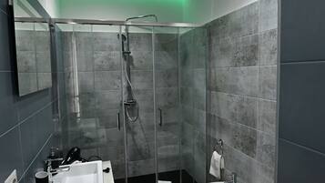 A modern bathroom with a glass-enclosed shower, a white sink, a bidet, and a toilet.