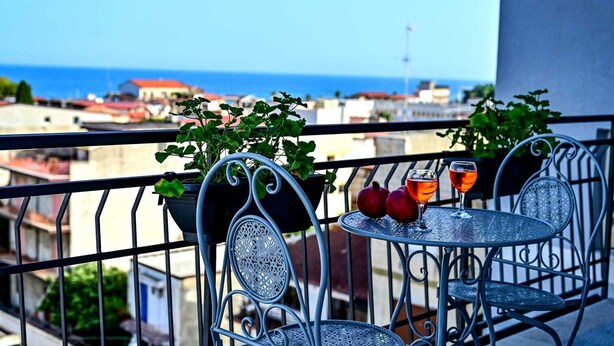 A balcony with two metal chairs and a small table, two pomegranates, and two glasses of orange liquid. - Kore suites&apartments (Locri)