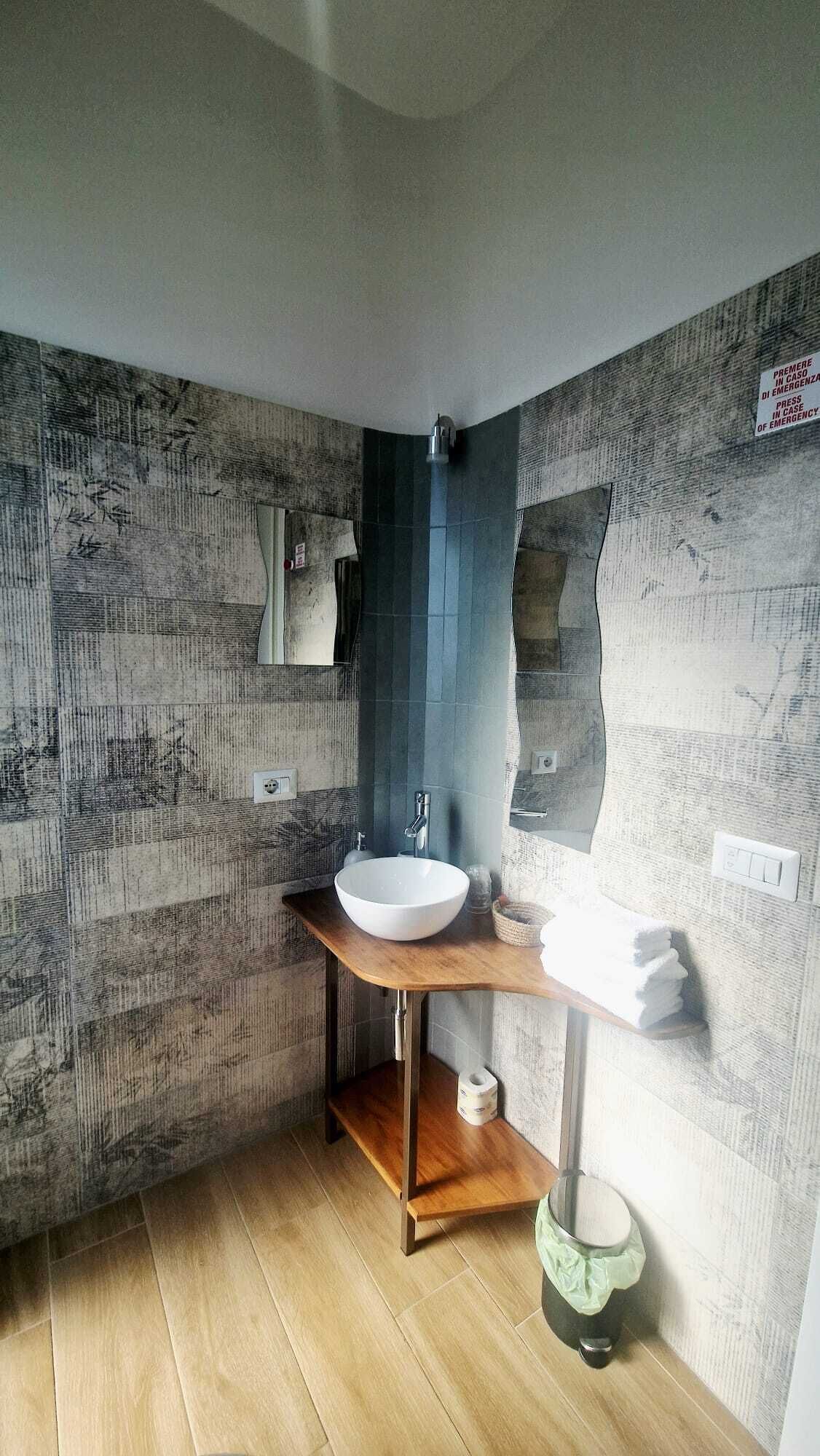 Un baño con tocador de madera, lavamanos blanco y cabina de ducha azul.