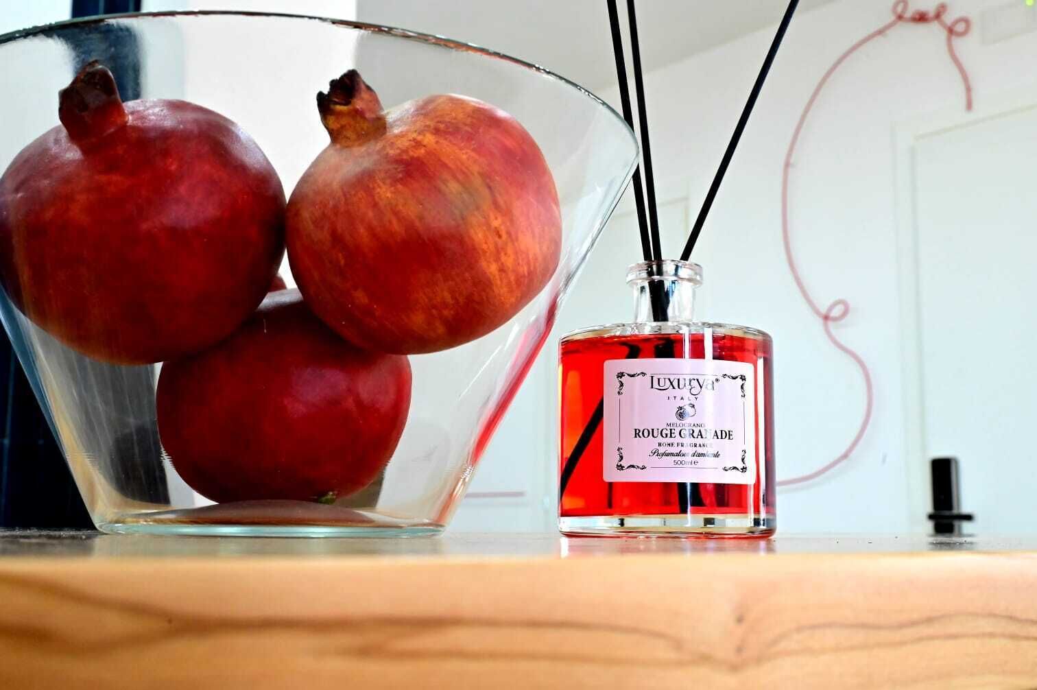 A glass bowl containing pomegranates and a bottle of Luxury Italia perfume.
