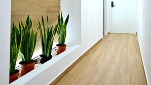 A modern hallway with wooden flooring and white walls, featuring a built-in planter with green plants. - Kore suites&apartments (Locri)