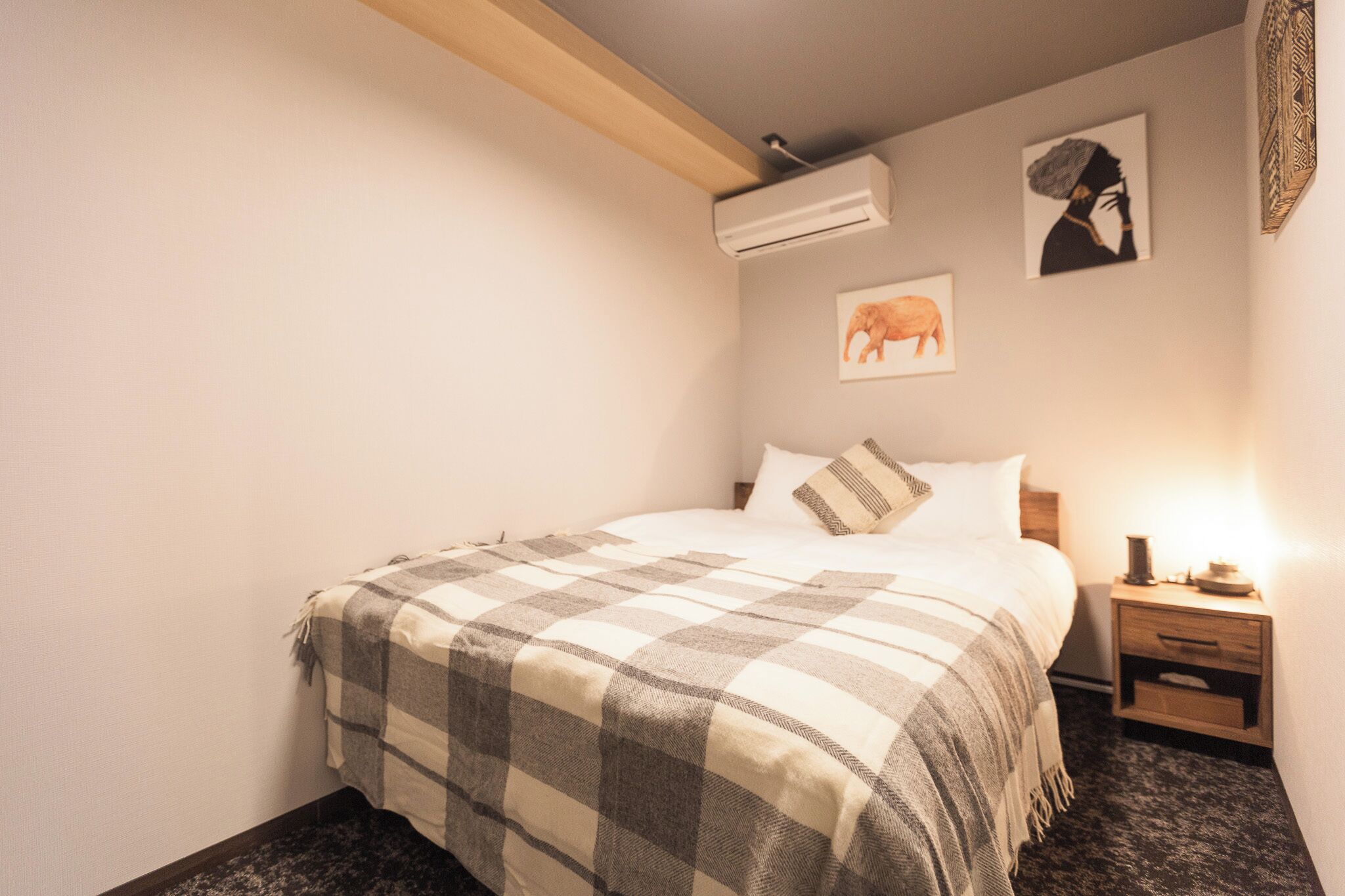 A bedroom with a bed, a nightstand, an air conditioner, and wall art.