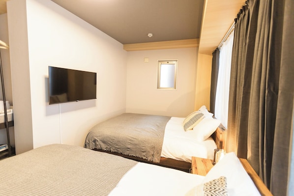 Une chambre d’hôtel avec un lit, un téléviseur fixé au mur, une petite fenêtre et une table de chevet.