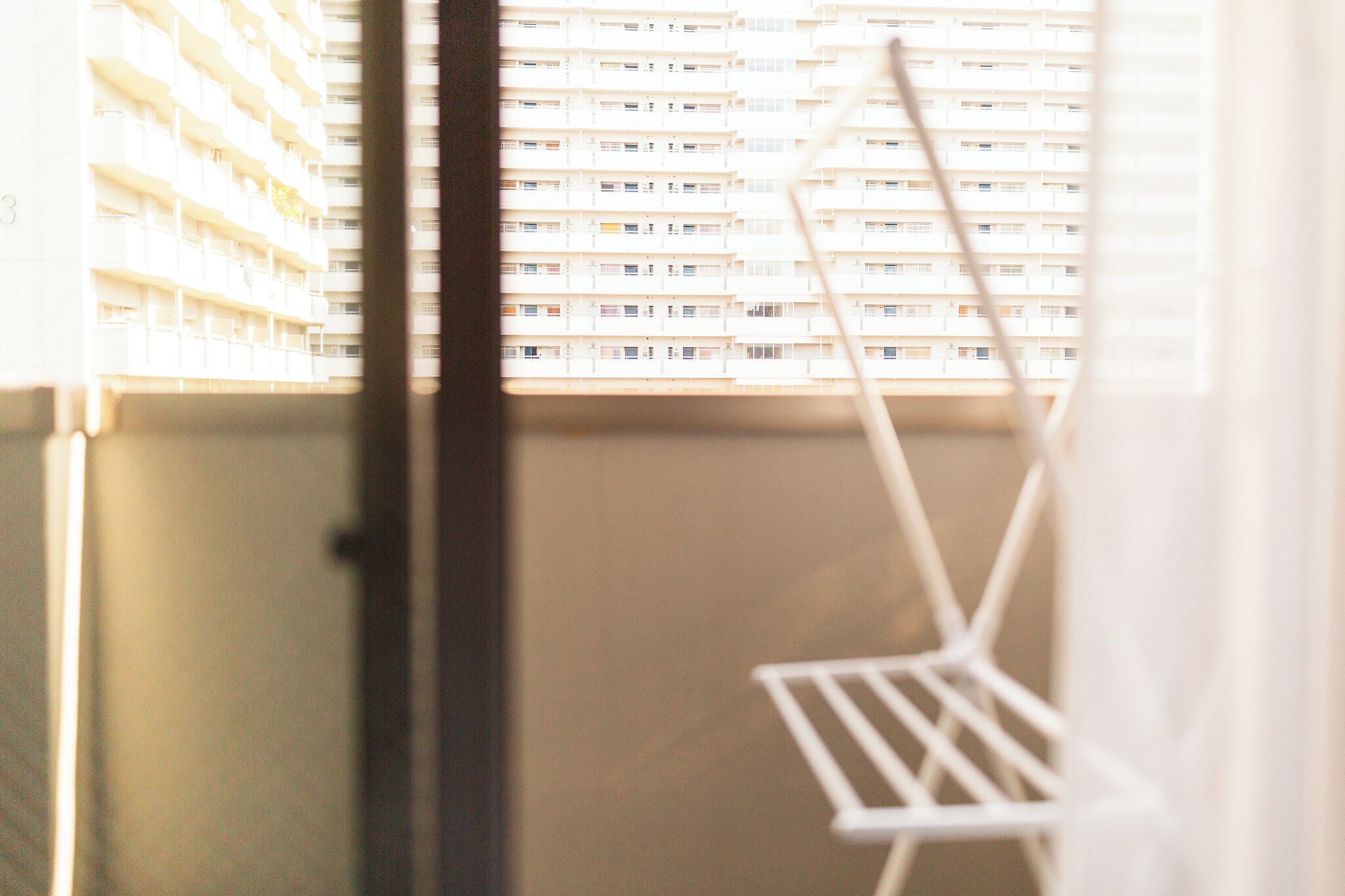 A balcony with a white chair, a building with multiple balconies in the background, and a window frame.