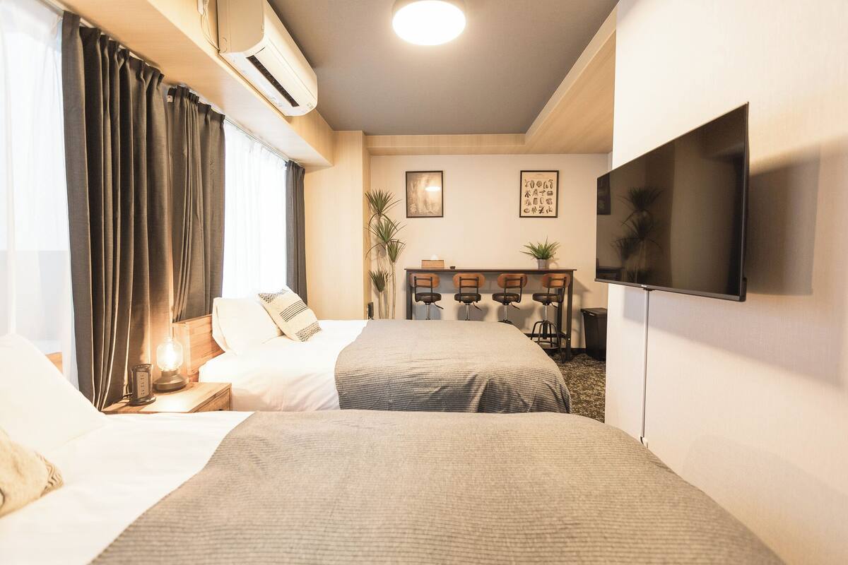 A hotel room with two beds, a TV, a desk, and a plant.