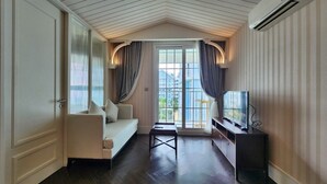 Ein Hotelzimmer mit einer Couch, einem kleinen Tisch, einem Fernseher und einem Balkon mit Vorhängen.
