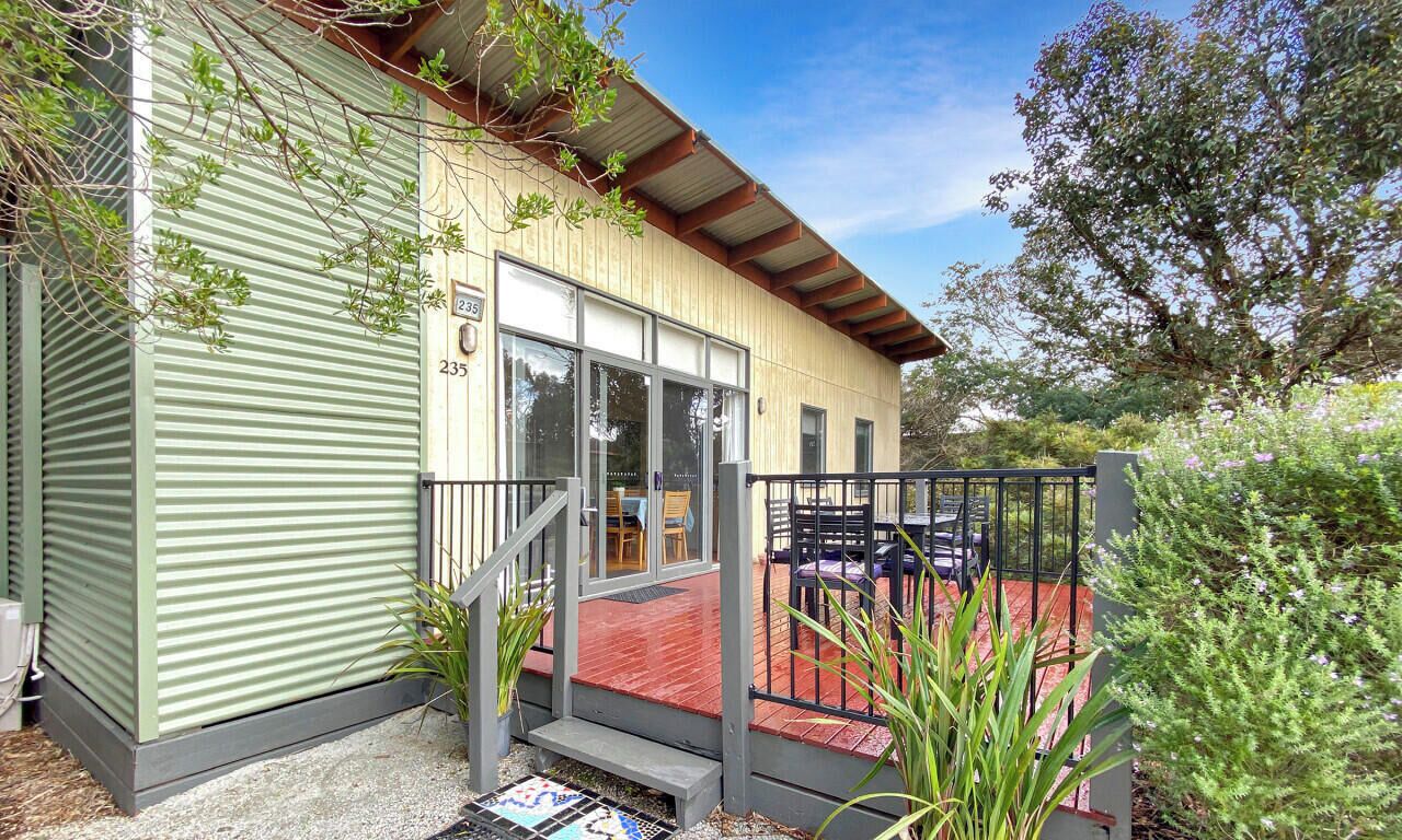 A coastal retreat with a green exterior, a red deck, and a gated entrance.