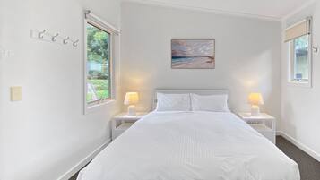 Une chambre à coucher blanche avec un lit, deux tables de chevet avec des lampes, un tableau au mur et une fenêtre sur le côté gauche.