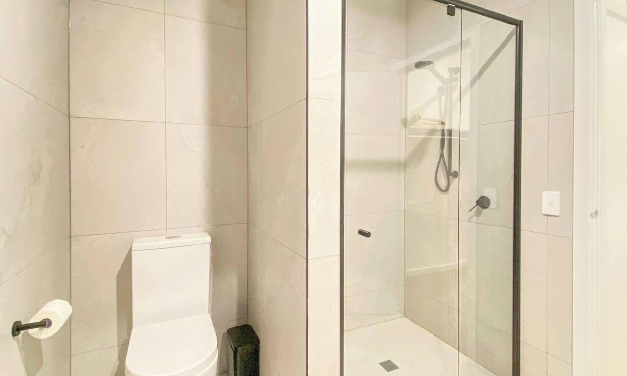 A modern bathroom with a toilet, a glass-enclosed shower area, and a tiled floor.