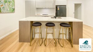 Uma cozinha moderna com bancada de mármore, três banquetas, uma geladeira e um revestimento de backsplash em padrão herringbone.