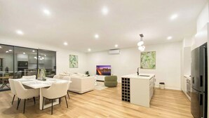 Uma sala de estar moderna com área de refeições, cozinha e uma grande tela de TV.