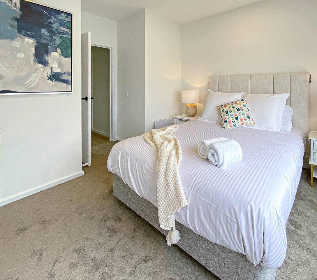 A bedroom with a large bed, two bedside tables, a headboard, and a painting on the wall.
