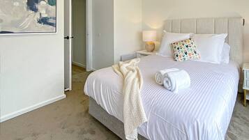 A bedroom with a large bed, two bedside tables, a headboard, and a painting on the wall.