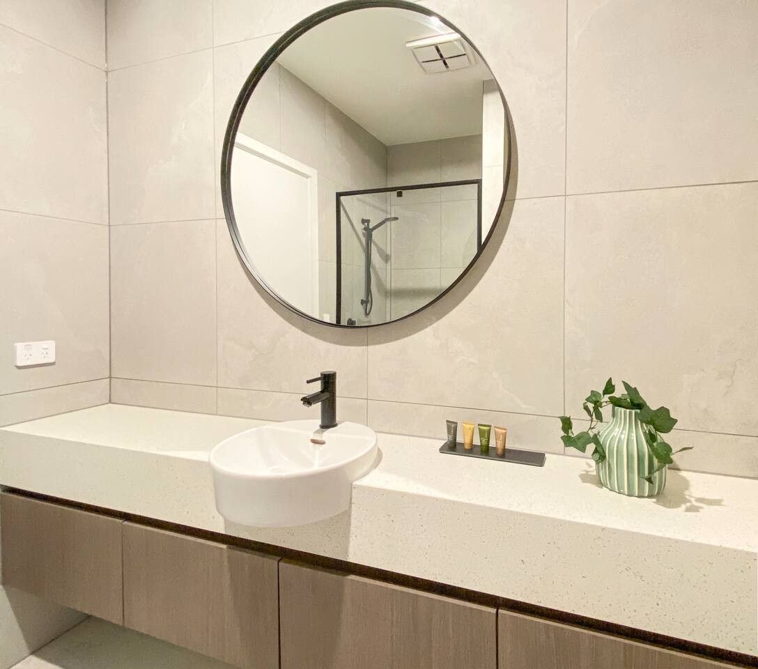 A bathroom with a round mirror, a white sink, and a shower area.