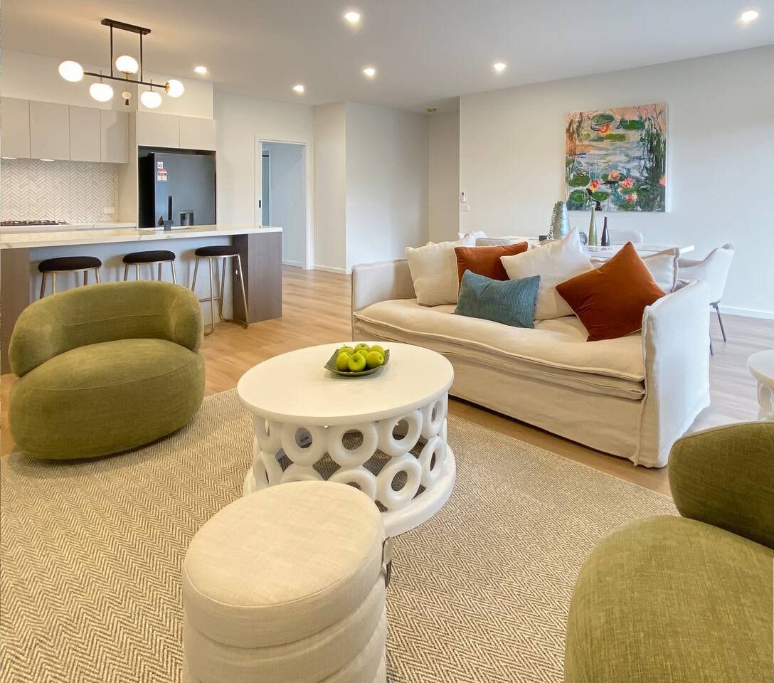 Un salon moderne avec un canapé, des poufs et une table basse. Il y a également un coin cuisine équipé d’un réfrigérateur et de tabourets de bar.