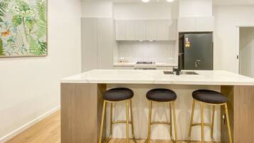 A modern kitchen with a marble countertop, three bar stools, a refrigerator, and a herringbone backsplash.