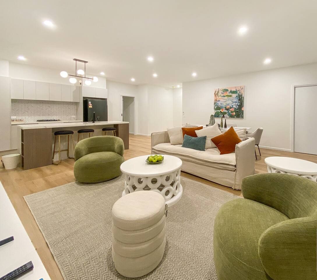 Een moderne woonkamer met een bank, groene fauteuils, een salontafel en een keuken op de achtergrond.