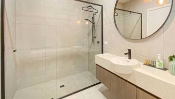 A modern bathroom with a glass-enclosed shower, a round mirror, and a vanity with a sink and toiletries.