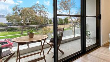 A balcony with a wooden table and chairs, a potted plant, and a white decorative stool.