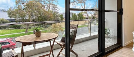 Un balcon avec une table et des chaises en bois, une plante en pot et un tabouret décoratif blanc.