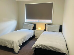 A twin room with two single beds, a nightstand with a lamp, and a window with blinds.