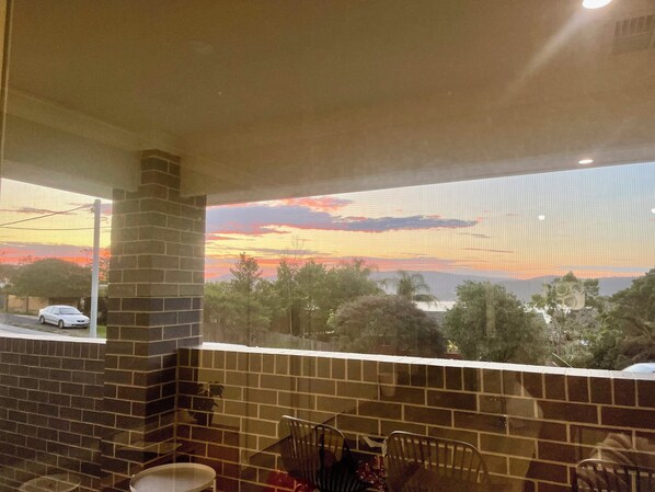 A room with a brick wall, a window overlooking a sunset, and a car parked outside.