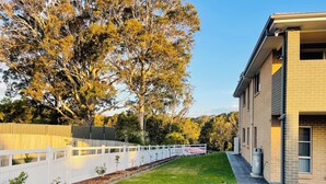 A residential property with a well-maintained lawn, a white picket fence, and mature trees. - Modern, comfortable with stunning Inlet-sunset-view Home in the heart of Narooma (Narooma)