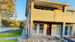 A modern two-story house with a brick facade, large windows, and a stone border around the lawn. - Modern, comfortable with stunning Inlet-sunset-view Home in the heart of Narooma (Narooma)