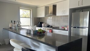 A modern kitchen with a central island, stainless steel appliances, and a window providing natural light. - Modern, comfortable with stunning Inlet-sunset-view Home in the heart of Narooma (Narooma)