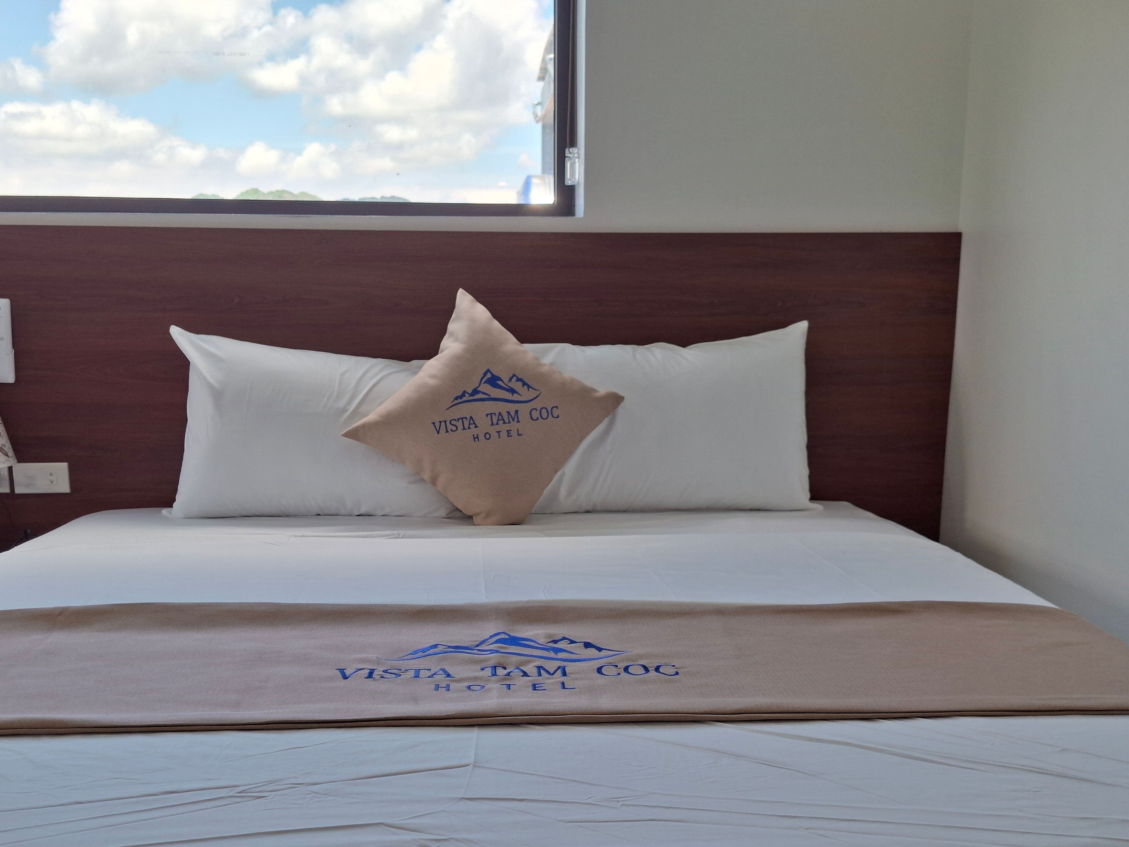 A hotel room with a bed, pillows, and a blanket with the hotel's logo.