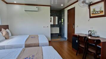 Camera d'albergo con due letti, una scrivania, una sedia, un ventilatore e un angolo cottura sullo sfondo.
