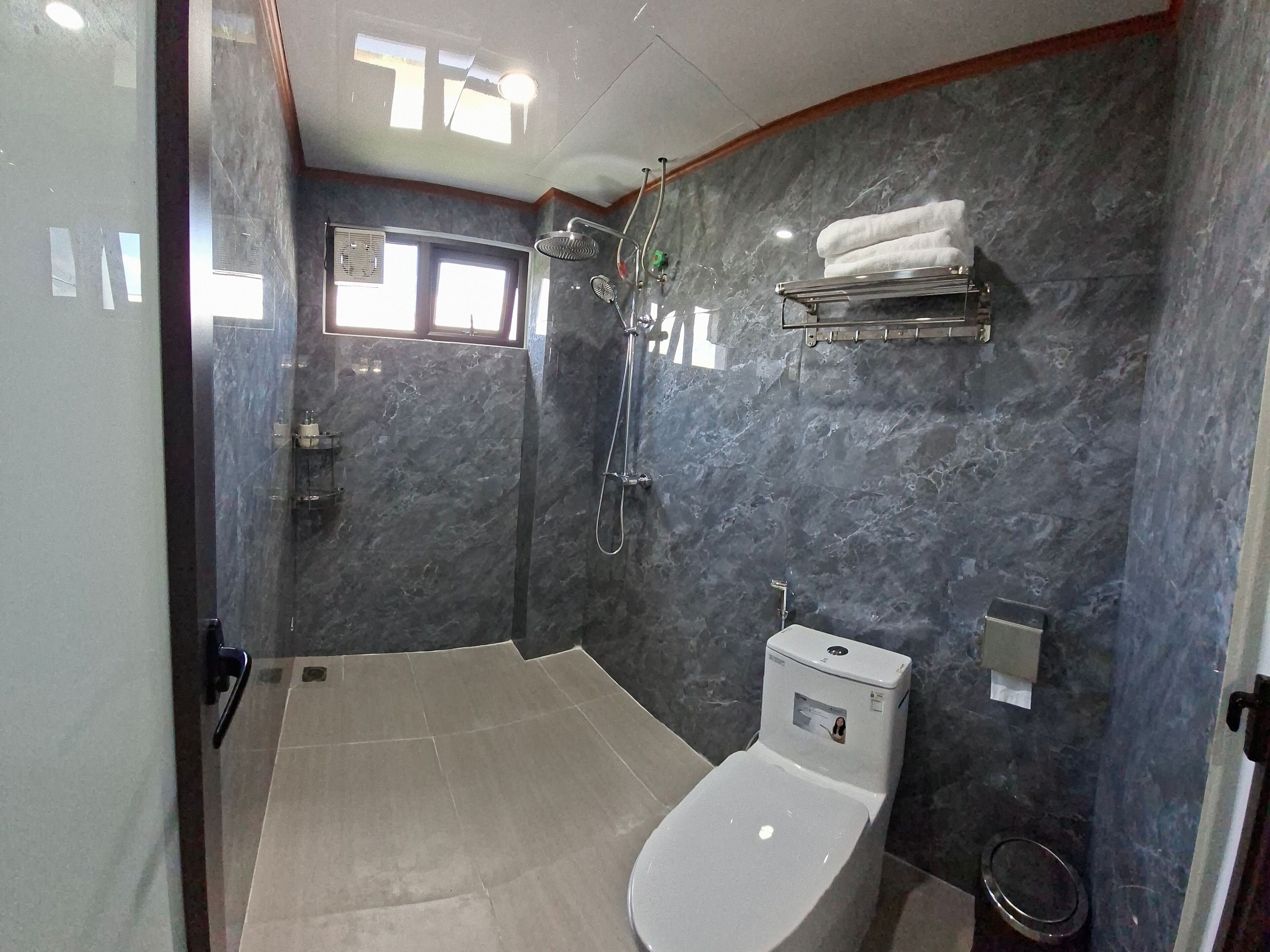 Ein modernes Badezimmer mit Toilette, Dusche mit Duschbrause, Handtuchhalter und einem Fenster für natürliches Licht.