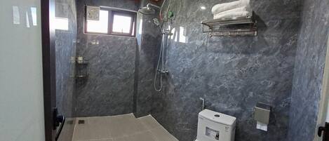 Ein modernes Badezimmer mit Toilette, Dusche mit Duschbrause, Handtuchhalter und einem Fenster für natürliches Licht.