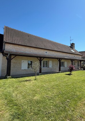 A stone building with a tiled roof, a small tree, and a clear blue sky.