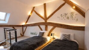 A loft bedroom with exposed wooden beams, a skylight, and a bed with a dark blanket.