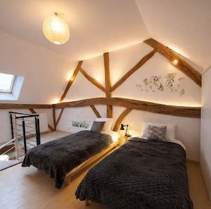 A loft bedroom with exposed wooden beams, a skylight, and a bed with a dark blanket.