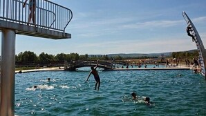 A swimming pool with a bridge, people swimming, and a person diving.