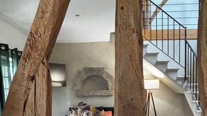 A rustic interior with exposed wooden beams, a stone fireplace, a staircase, and a view of the outdoors.