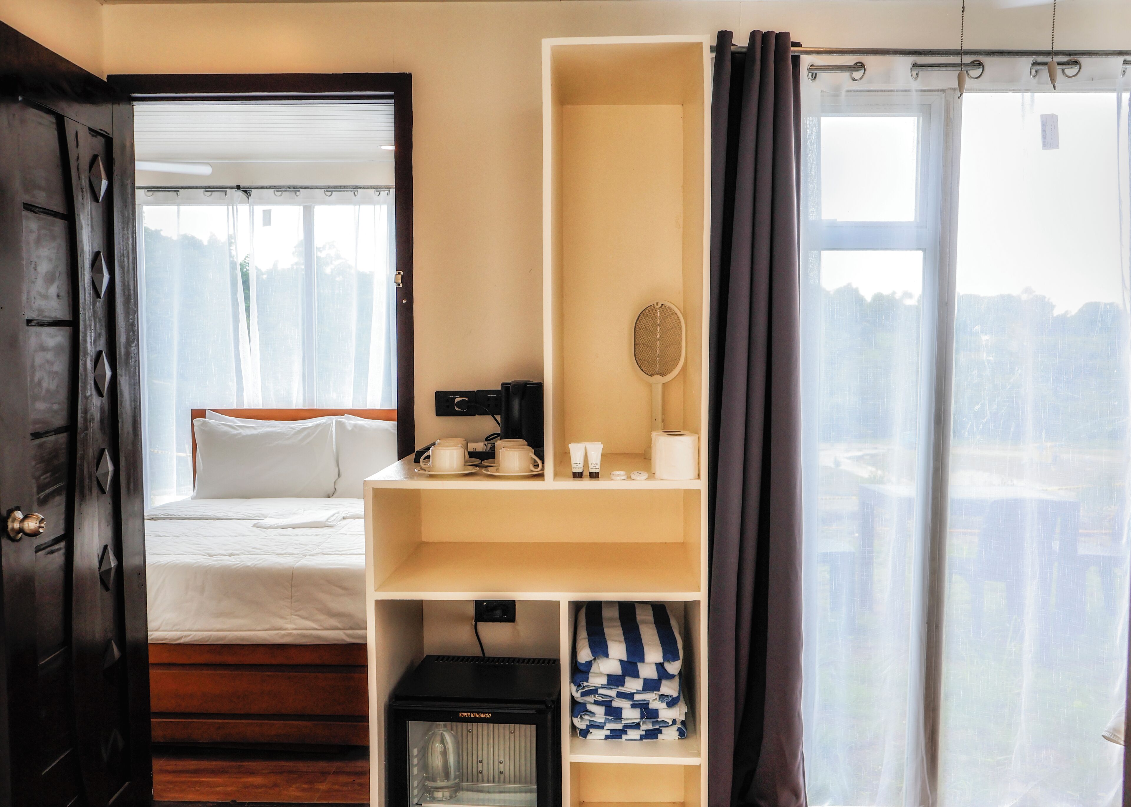 A hotel room with a bed, a desk with a kettle, a tennis racket, and a view of the city.
