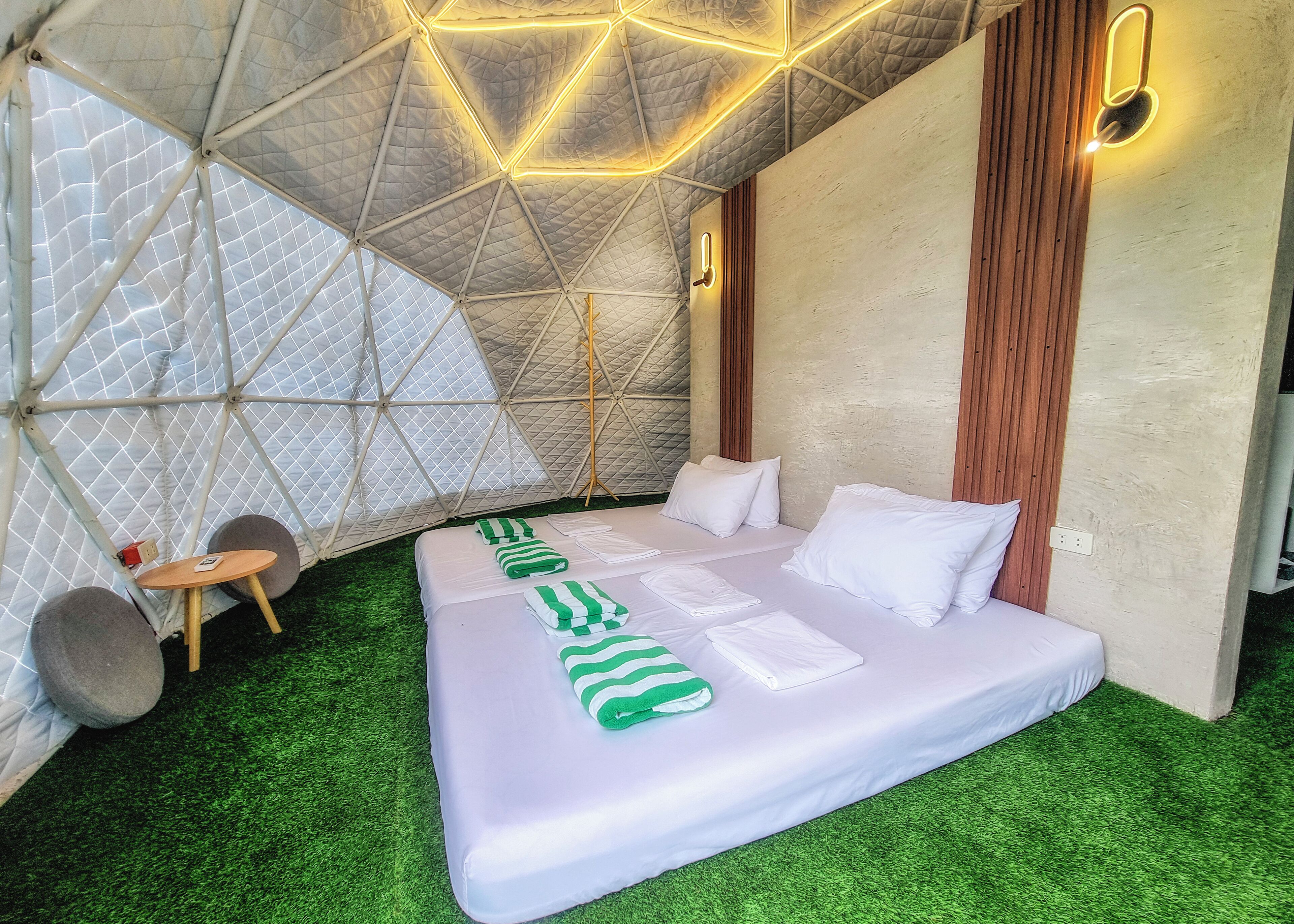 Une chambre moderne, au décor géométrique, comprenant un lit, une moquette verte synthétique et un plafond à la structure originale.
