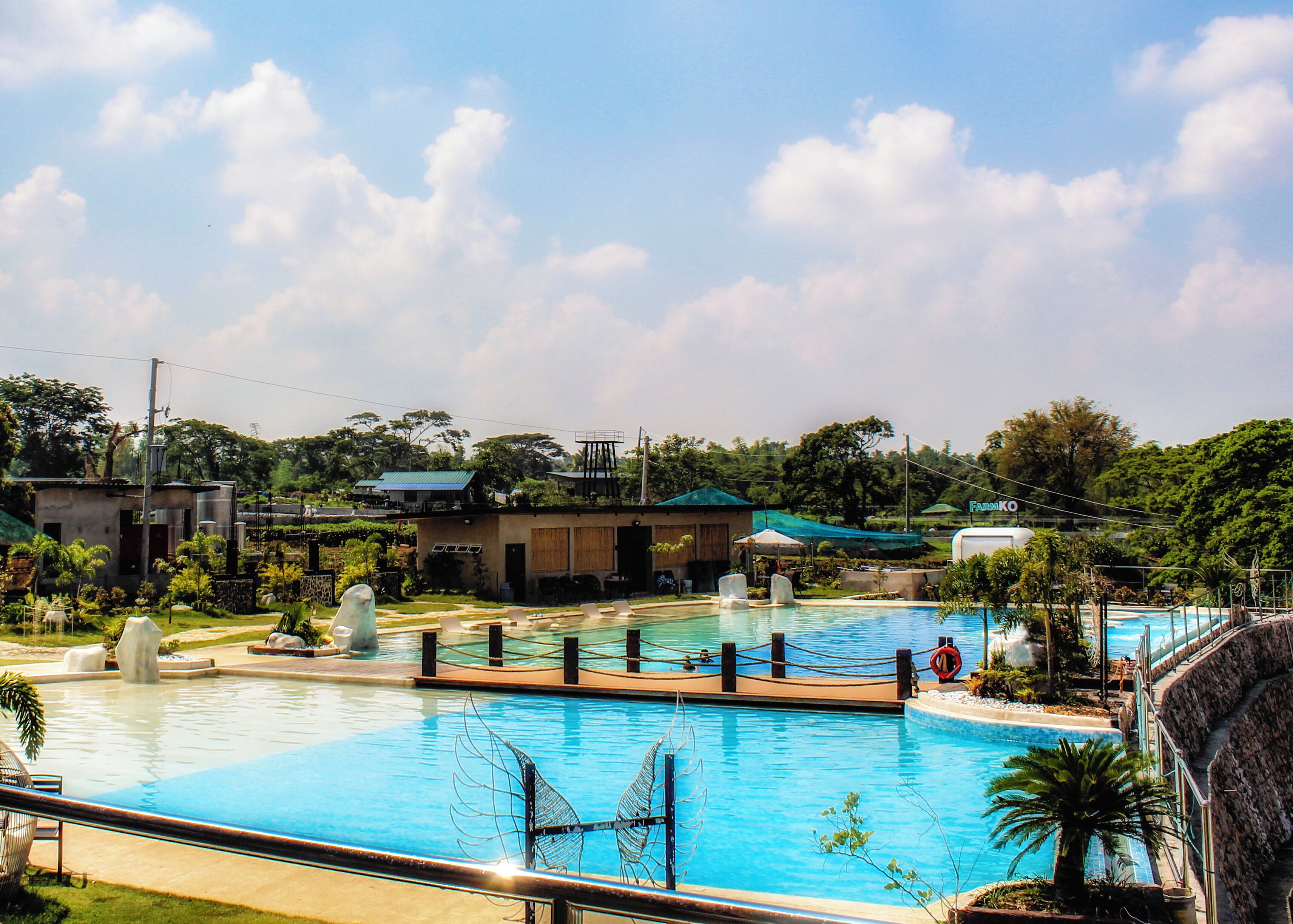 Una piscina con sillones de descanso, una fuente de agua y vistas de edificios y zonas verdes circundantes.