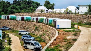 A series of dome-shaped mobile homes arranged in rows, with a stone retaining wall and a dirt path leading to a parking area. - FarmKo Glamping (Dolores)