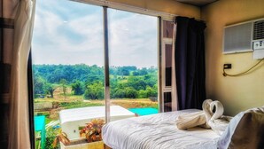 Ein Hotelzimmer mit großem Fenster, einem Bett mit weißer Bettwäsche und Blick auf eine grüne Landschaft.